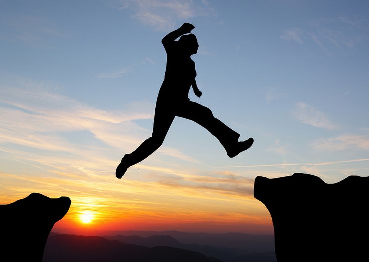 Silhouette Of Hiking Man Jumping Over The Mountains At Sunset